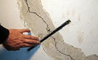 A wall with a large crack is being inspected by a professional in Arlington, TX
